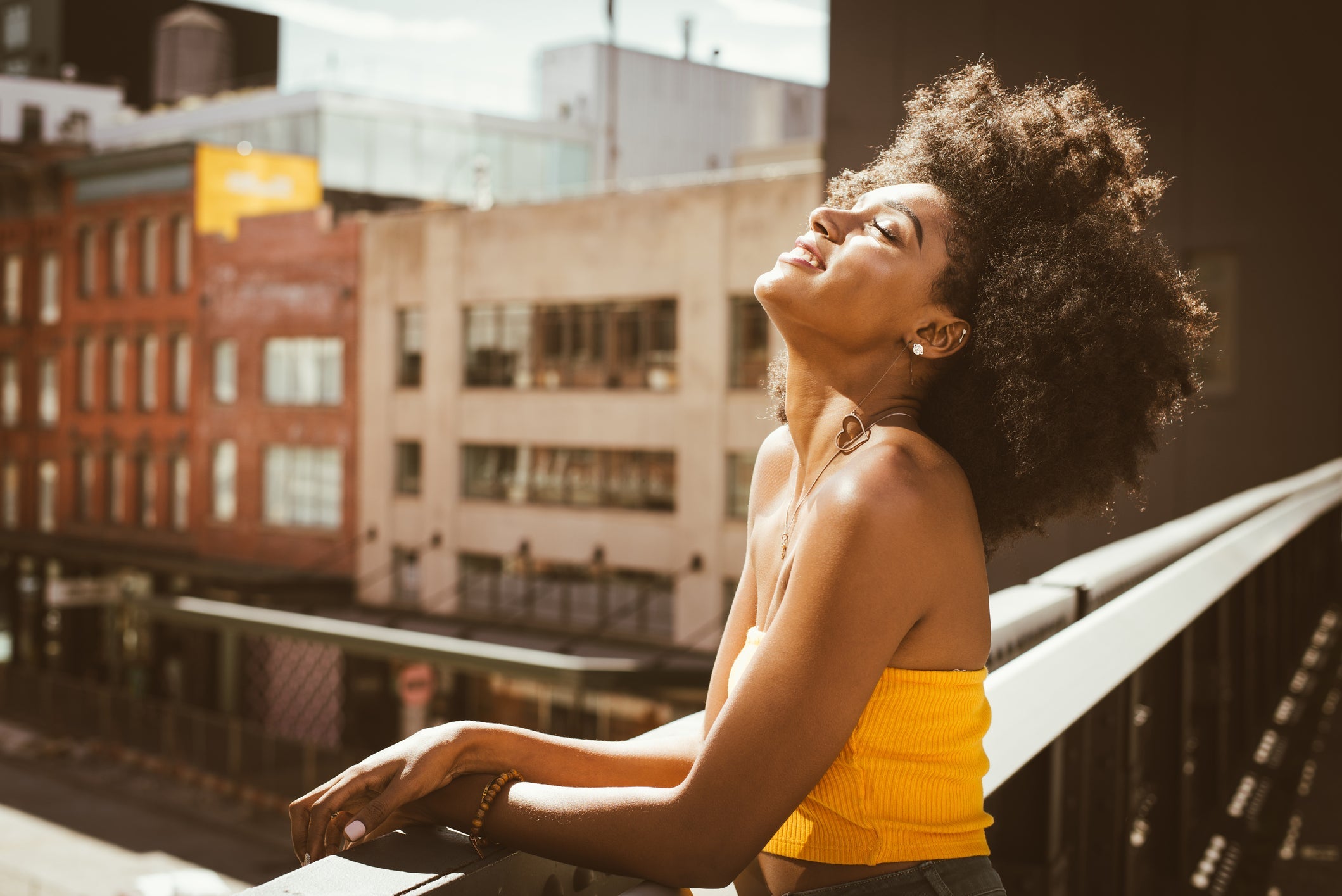 woman with curly hair wearing yellow top on the balcony taking in the son