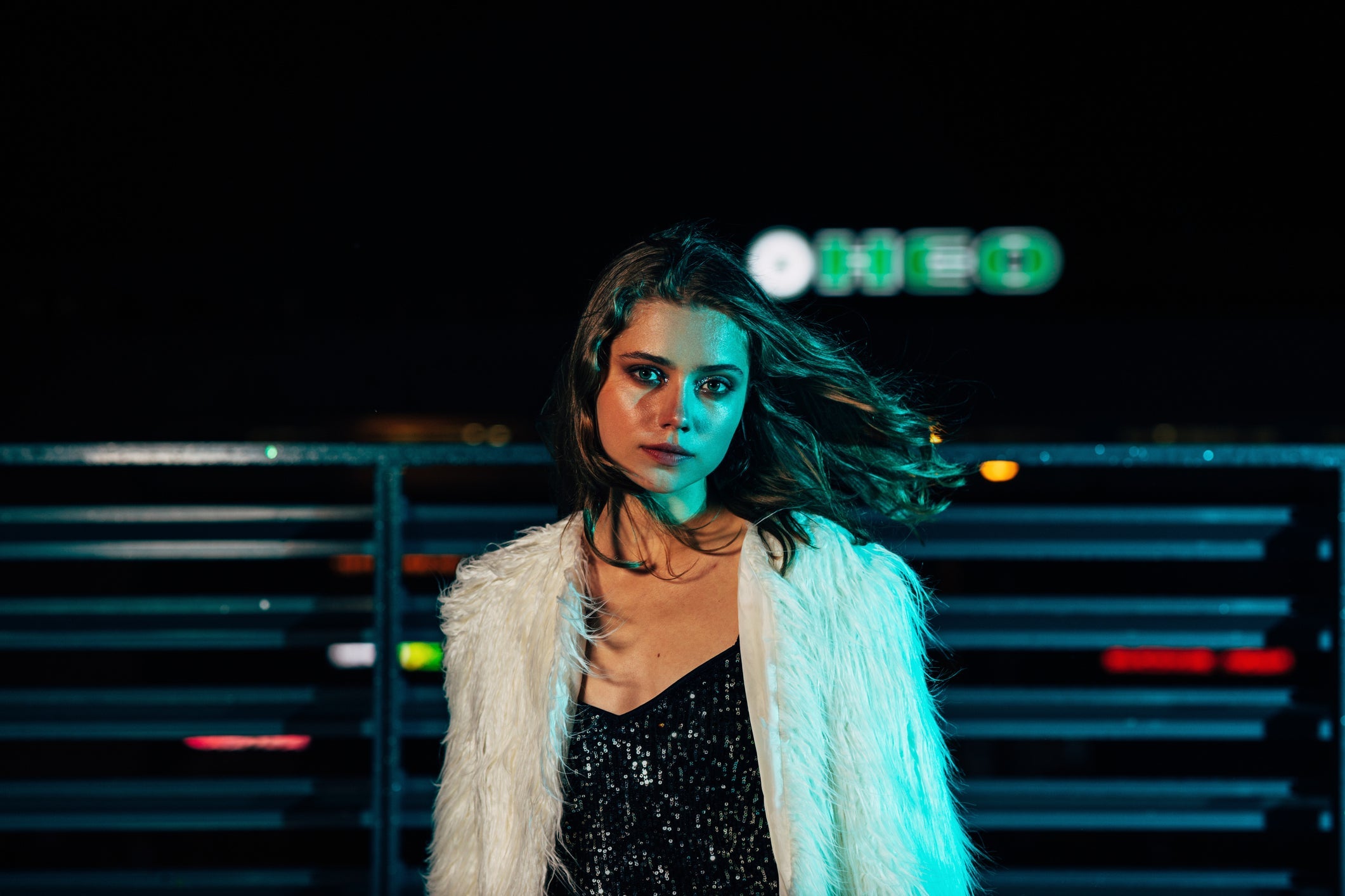woman with feather jacket and sparkling black dress posing at night with hair blowing in the wind